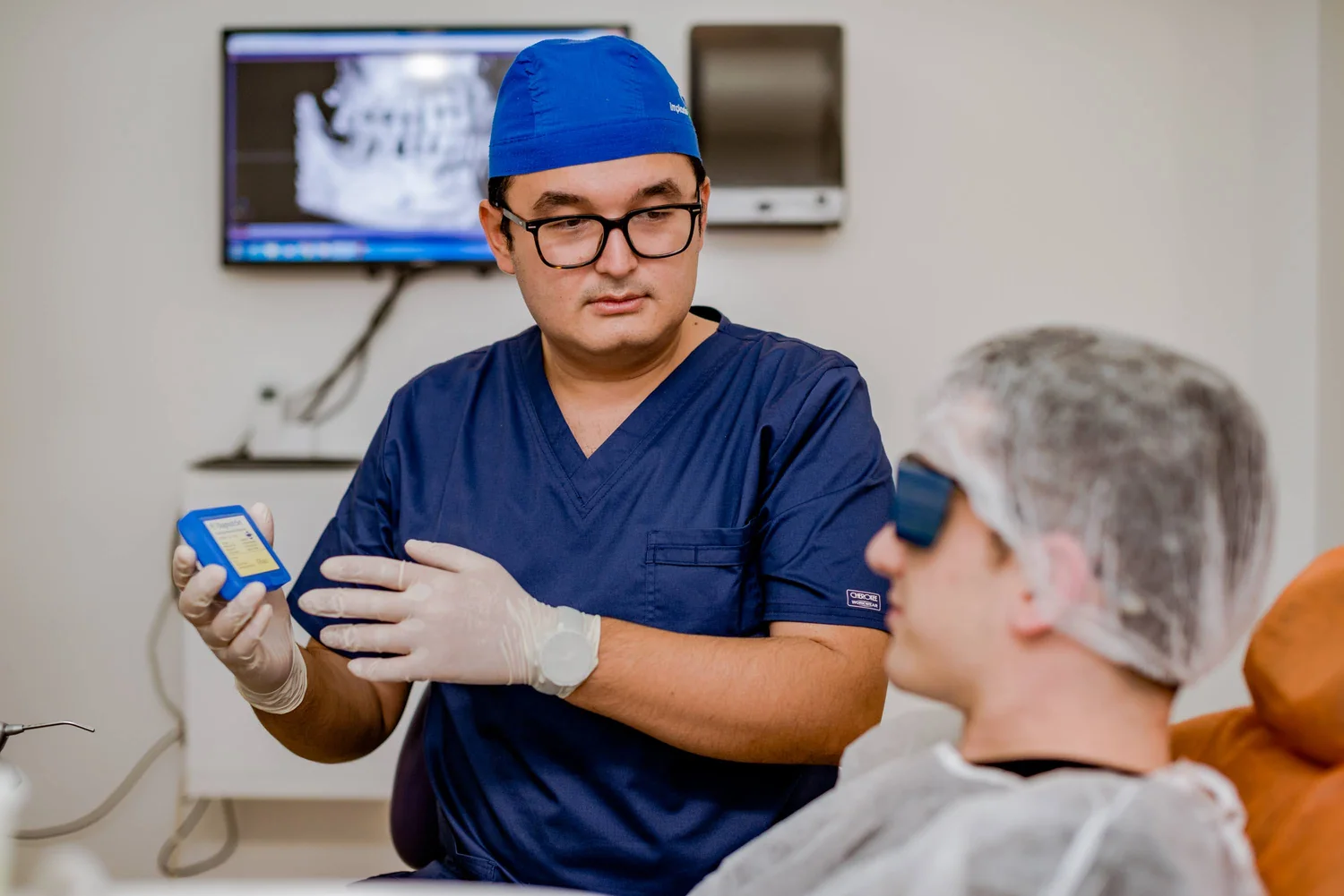 Dr. Olgun Chemal îi arată unui pacient un implant dentar, explicând tratamentul